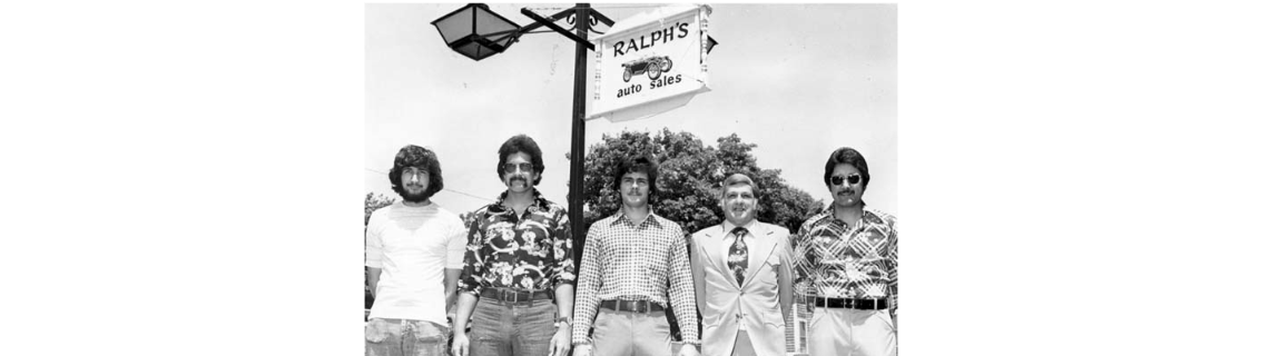 Phillip, Mark, Ralph Jr., Ralph Sr., and David Medeiros standing beneath a Ralph's Auto Sales sign, left to right